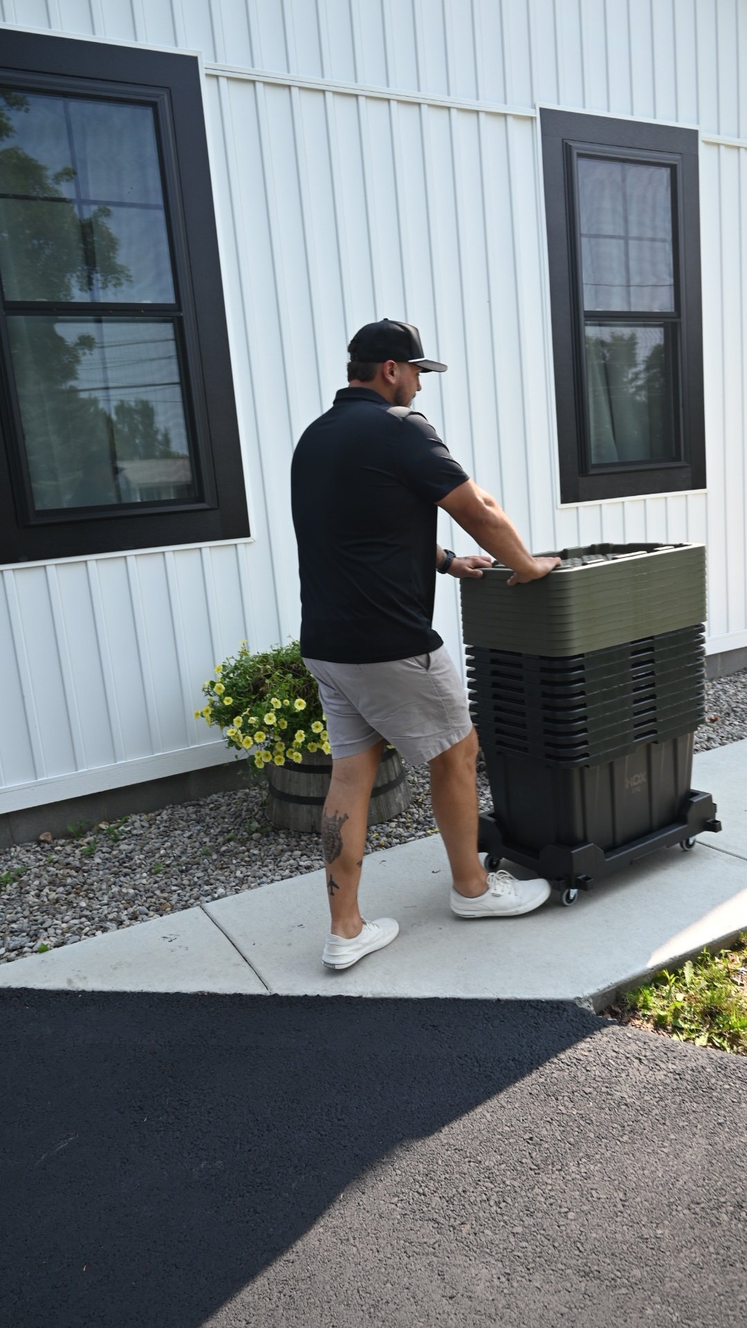Man pushing collapsed rental totes stacked on a dolly walking down the sidewalk to customer house 