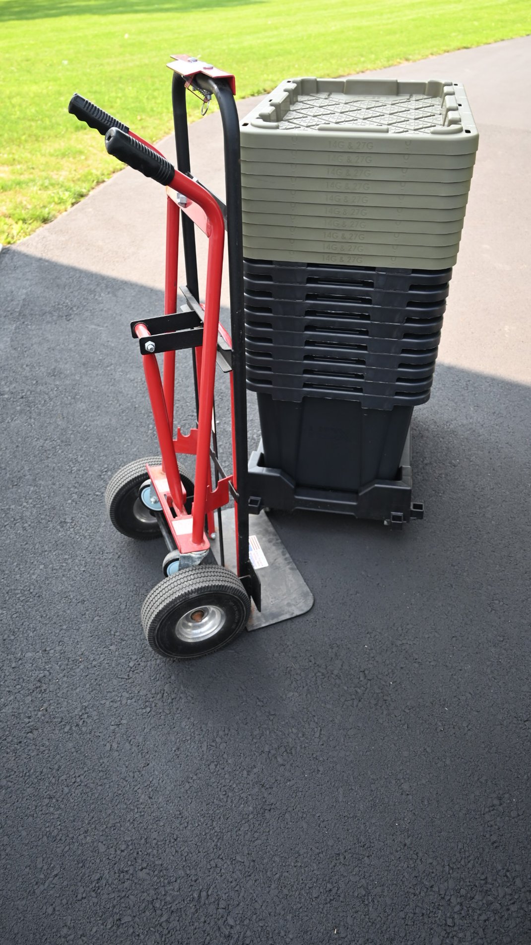 Collapsed black and green rental totes on top of dollies and pictured with hand truck